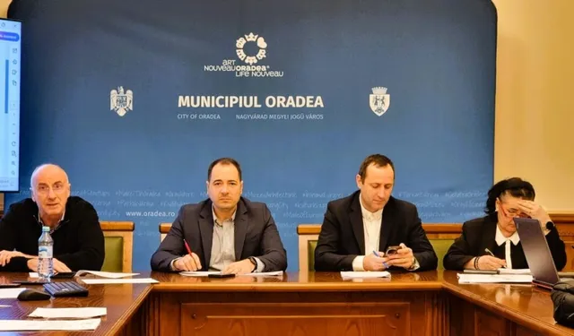 Patru bărbați stau la o masă de lemn în fața unui panou albastru pe care scrie Municipiul Oradea.