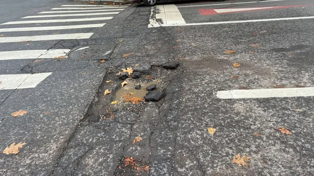 O groapă cu apă se află pe asfaltul unei străzi lângă marcajele de trecere a pietonilor.