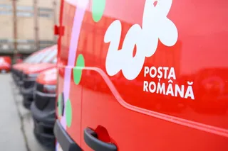 Un vehicul roșu cu inscripția albă Poșta Română este parcat pe o stradă lângă alte mașini de culoare roșie.