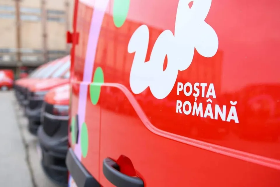 Un vehicul roșu cu inscripția albă Poșta Română este parcat pe o stradă lângă alte mașini de culoare roșie.