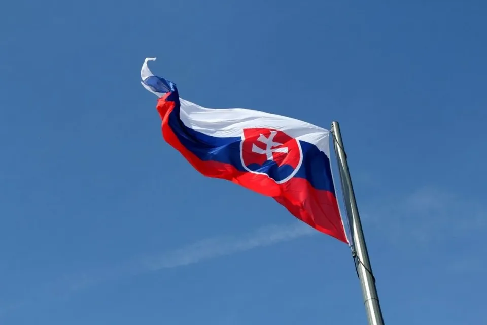 Steagul Slovaciei flutură pe un stârf metalic sub un cer albastru.
