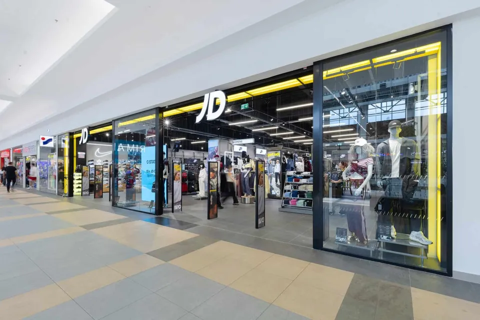 O fațadă de magazin cu un logo negru pe fundal alb este situată într-un centru comercial cu podea de gresie și vitrine mari de sticlă.