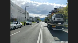 Un autovehicul alb este ridicat de pe asfalt de către un camion cu platformă pe un drum urban cu marcaje albe.