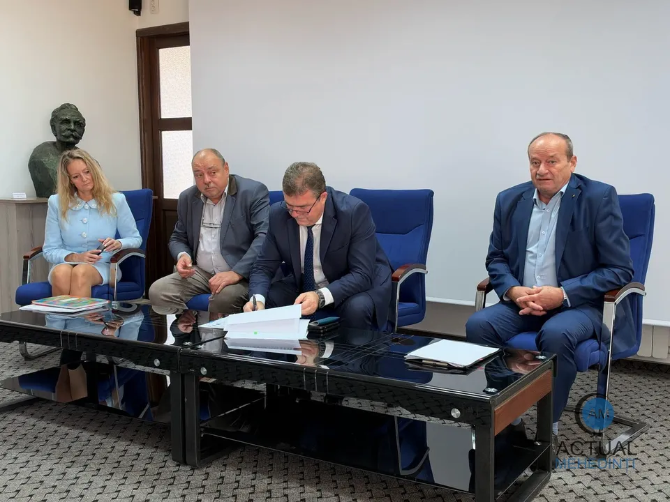 Patru bărbați și o femeie stau la o masă neagră într-o încăpere cu un bust pe un soclu în fundal.