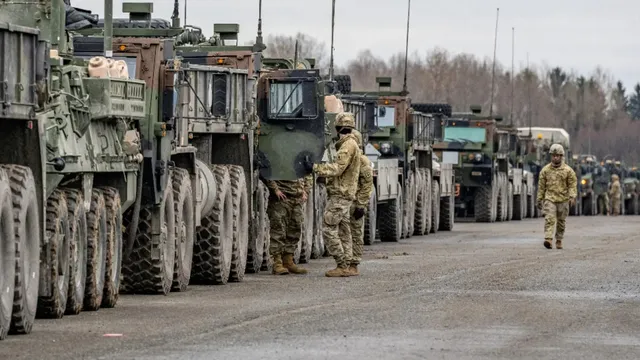 O linie de vehicule militare verzi este parcată pe un drum, în timp ce câțiva militari în uniforme de camuflaj stau lângă acestea.
