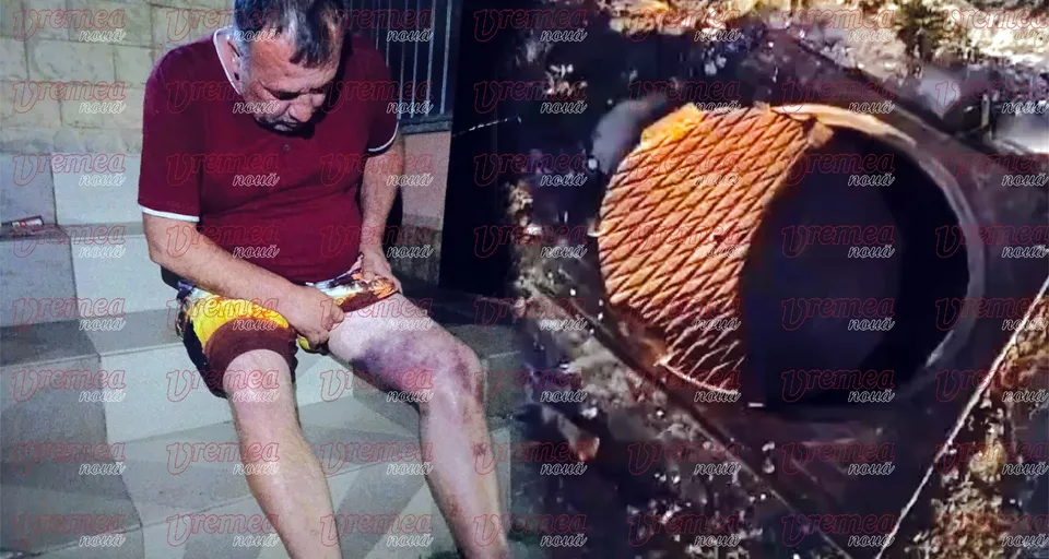 Un bărbat cu un tricou roșu și pantaloni scurți galbeni stă așezat pe o treaptă lângă o gaură deschisă în asfalt cu un capac de canalizare întors.
