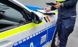 Un agent de poliție în uniformă scrie pe o foaie de hârtie de pe capota unui autoturism marcat cu culori de serviciu.