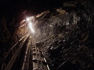 O rampă de transport metalică cu role parcurge un tunel întunecat lângă un perete de stâncă și pietriș.