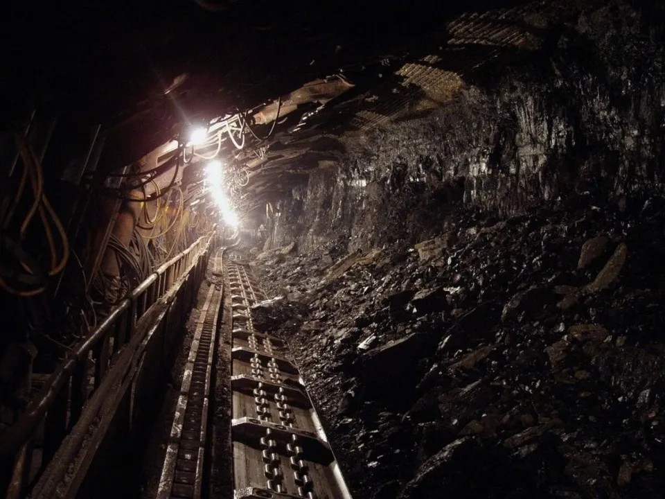 O rampă de transport metalică cu role parcurge un tunel întunecat lângă un perete de stâncă și pietriș.