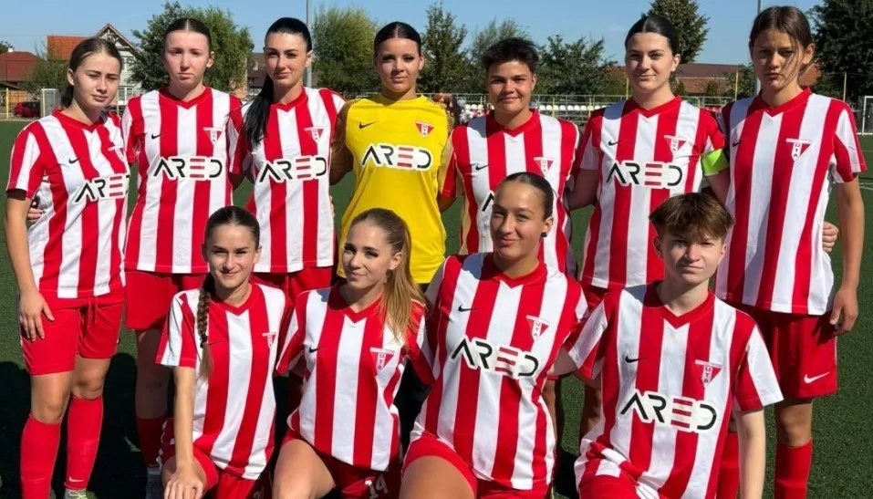 Un grup de femei poartă echipamente sportive cu dungi verticale roșii și albe, în timp ce o jucătoare poartă un echipament galben.
