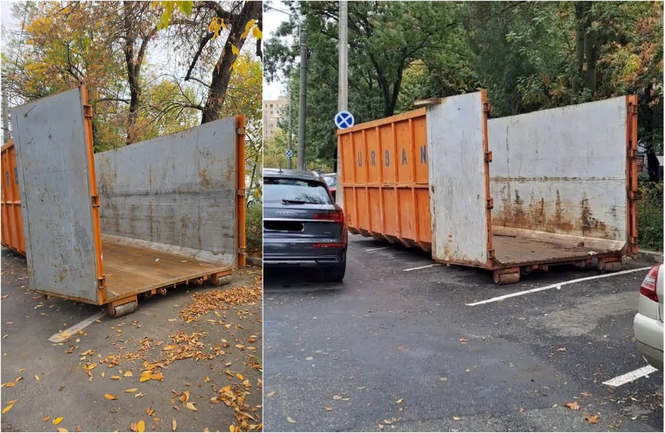 Două containere metalice portocalii și gri sunt amplasate pe un drum asfaltat lângă mașini și copaci.