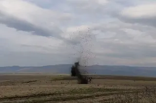 O coloană de praf și resturi este proiectată în aer de pe un câmp deschis sub un cer înnorat.