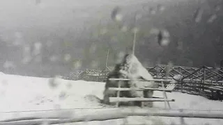 O bancă de lemn acoperită de zăpadă se află pe un teren deszăpezit sub un cer gri și întunecat.