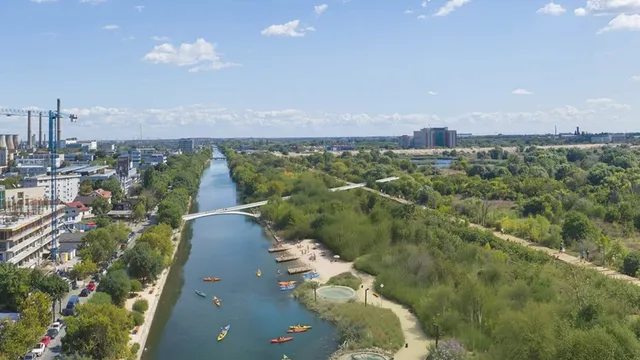 O vedere aeriană a unui canal cu apă, flancat de o zonă urbană cu clădiri și o zonă verde cu copaci și un ponton.