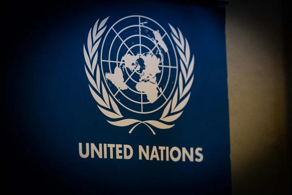Logo-ul alb al Națiunilor Unite este afișat pe un fundal albastru sub textul alb 'UNITED NATIONS'.