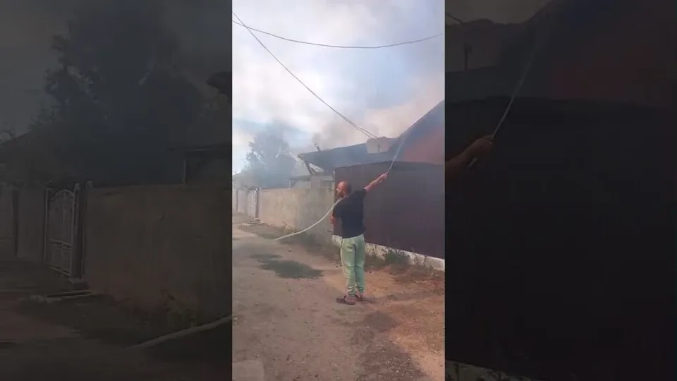 Un bărbat cu pantaloni deschiși și tricou închis de culoare ține un cablu întins deasupra unei clădiri sub un cer înnorat.