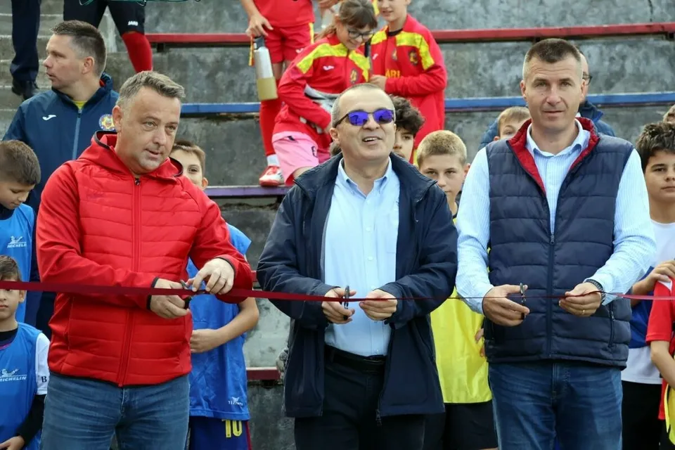 Trei bărbați stau în linie și țin o panglică roșie întinsă în fața lor, în timp ce alți oameni stau în spatele lor pe trepte.