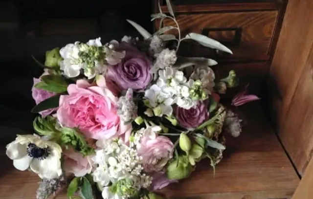 Un buchet de flori roz și albe cu frunze verzi este așezat pe o suprafață de lemn lângă un sertar maro.