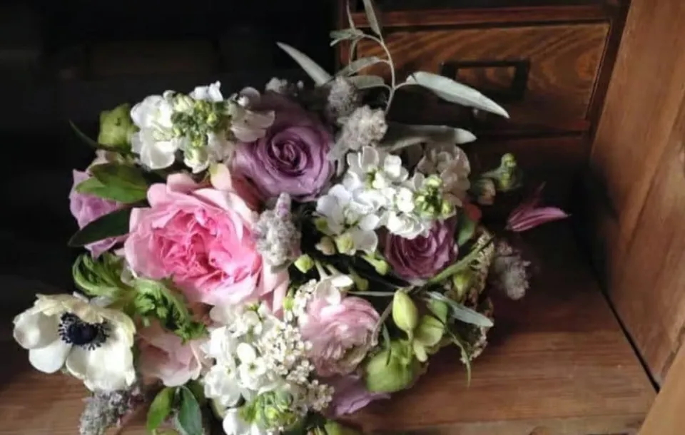 Un buchet de flori roz și albe cu frunze verzi este așezat pe o suprafață de lemn lângă un sertar maro.