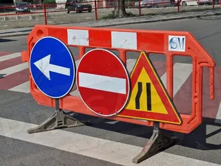 Trei semne de circulație rutiere sunt montate pe un bariera portocalie situată pe un drum asfaltat.