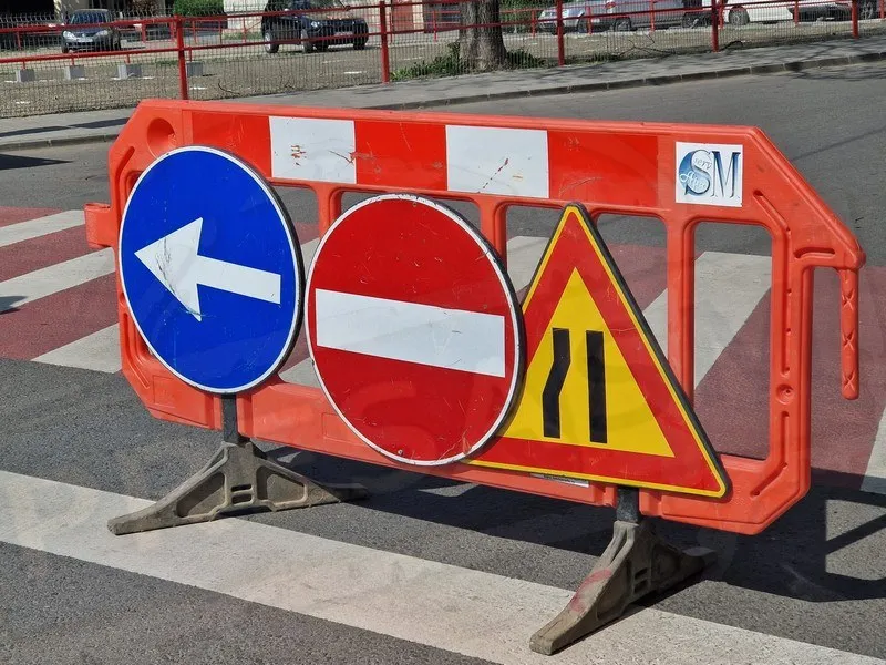 Trei semne de circulație rutiere sunt montate pe un bariera portocalie situată pe un drum asfaltat.