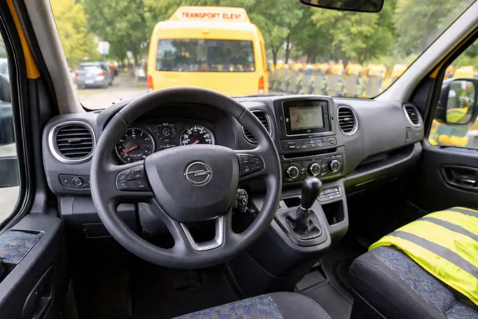 Interiorul unui vehicul cu volan, bord și o vestă reflectorizantă galbenă așezată pe scaunul pasagerului.