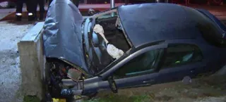 Un autoturism de culoare închisă este lovit de un stâlp de beton, având capota și partea frontală puternic deformate.