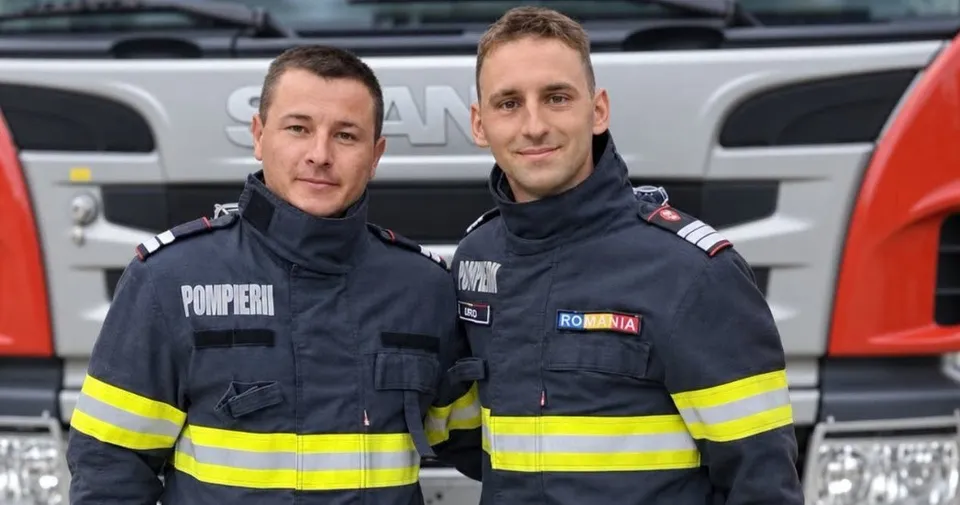 Doi bărbați în uniforme de pompieri cu benzi reflectorizante galbene stau în fața unui vehicul alb.
