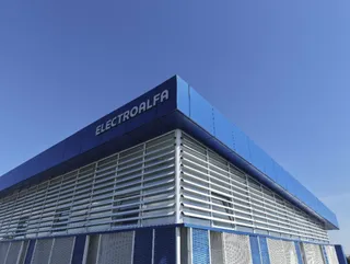 O clădire albastră cu panouri orizontale gri și un semn cu textul ELECTROALFA este situată sub un cer senin și albastru.