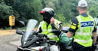 Un motociclist cu cască și vestă reflectorizantă stă pe o motocicletă lângă un polițist care poartă o vestă cu inscripția POLITA.