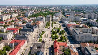 O vedere aeriană a unui oraș cu diverse clădiri rezidențiale, străzi cu mașini parcate și zone verzi cu copaci.