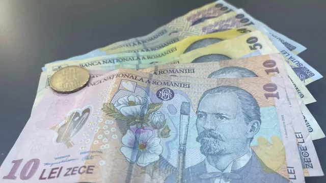 Mai multe bancnote românești și o monedă metalică sunt întinse pe o suprafață plană și gri.