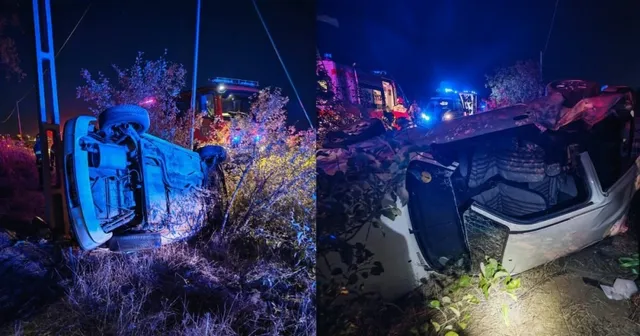 Un autoturism alb este răsturnat pe o parte într-un șanț cu vegetație, fiind iluminat de lumini de serviciu noaptea.