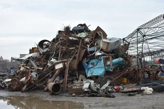 O grămadă mare de deșeuri metalice ruginite și obiecte din metal sunt amestecate pe un teren de afară sub un cer înnorat.