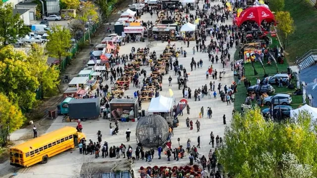 O mulțime de oameni merge pe un drum pavat lângă standuri, corturi albe și un autobuz galben parcat.