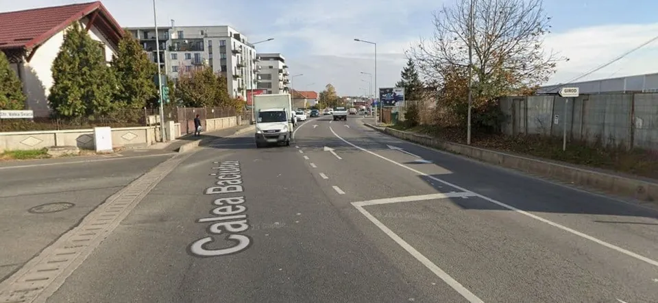 O stradă asfaltată cu marcaje albe prezintă un camion alb și clădiri în fundal sub un cer înzăpezit.