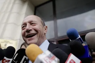 Un bărbat vârstnic zâmbește în fața mai multor microfoane de jurnalism îndreptate spre el.