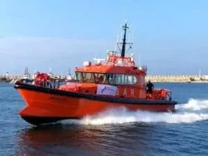O barcă de culoare portocalie navighează pe apă, lăsând în urmă un vârf de spumă albă sub un cer senin.