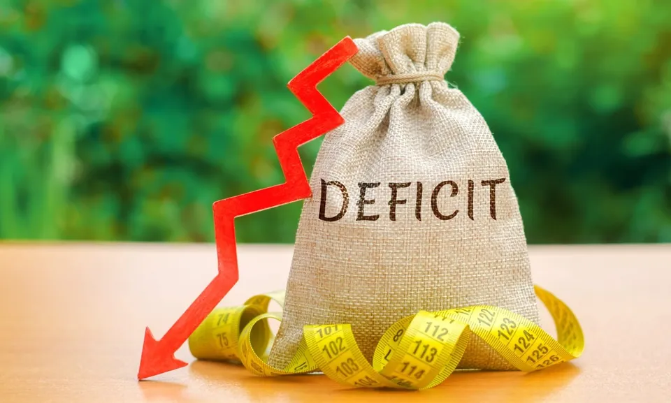 Un sac de pânie cu textul DEFICIT, un grafic roșu în formă de zig-zag și o centimetru de croitorie galben pe o suprafață plană.