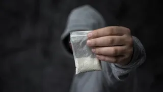 O persoană purtând un hanorac gri ține un plic mic transparent conținând o substanță albă pudră.
