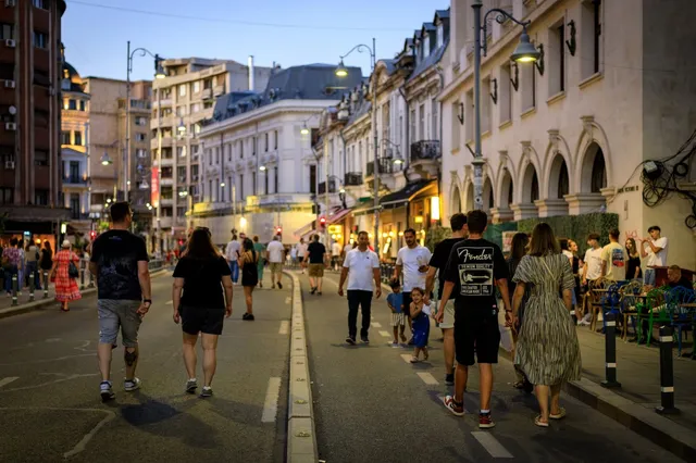 Oamenii merg pe o stradă urbană cu clădiri înalte și felinare aprinse în timpul serii.