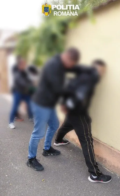 Două persoane întindute pe asfalt, una purtând pantaloni negri cu dungă albă și încălțăminte neagră, în timp ce o altă persoană este vizibilă în fundal.