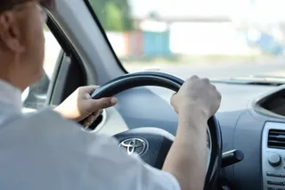 Un bărbat conduce un autoturism ținând volanul cu ambele mâini.