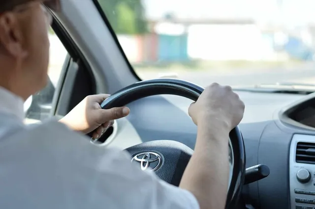 Un bărbat conduce un autoturism ținând volanul cu ambele mâini.