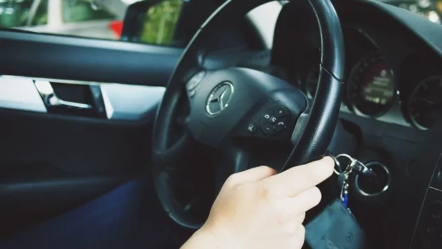 O mână ține o cheie introdusă în contactul unei mașini, lângă volanul cu emblema unei mărci auto.