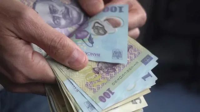 Mâinile unei persoane țin un teanc de bancnote de o sută de lei.