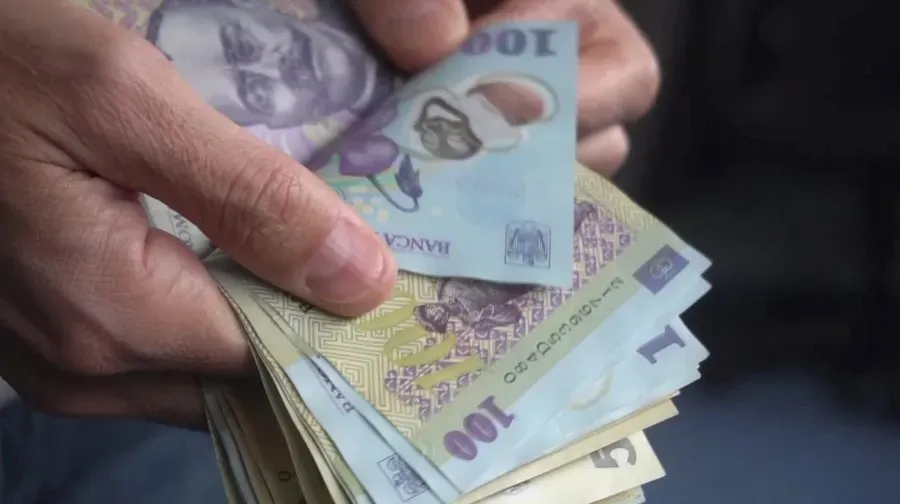 Mâinile unei persoane țin un teanc de bancnote de o sută de lei.