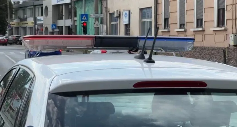 O mașină albă este surprinsă din spate, având pe plafon un bară de lumină cu culori roșu și albastru.