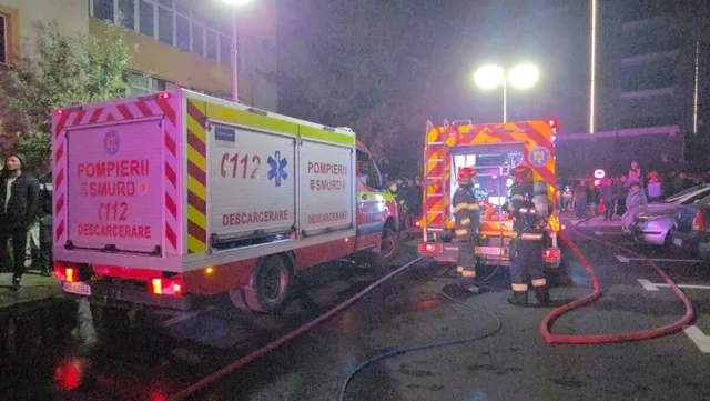 Două autospeciale de serviciu cu marcaje de pompieri sunt parcate pe un drum, lângă care se află furtunuri de apă întinse pe asfalt.