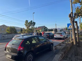 Două autoturisme negre și un sedan alb sunt parcate pe marginea unui drum asfaltat sub un cer senin.